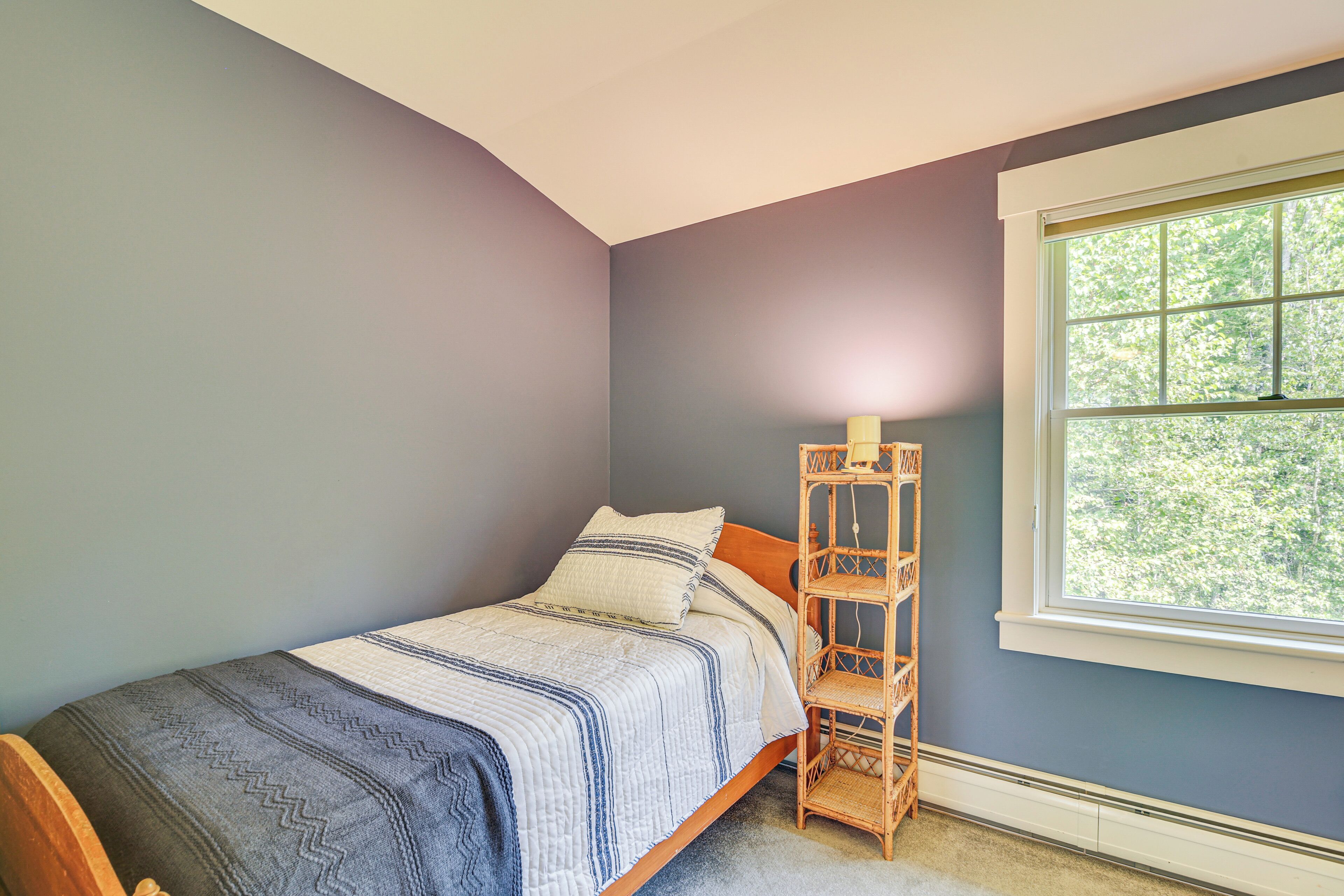 A bedroom with a bed, a nightstand, a window, and a wall-mounted shelf.