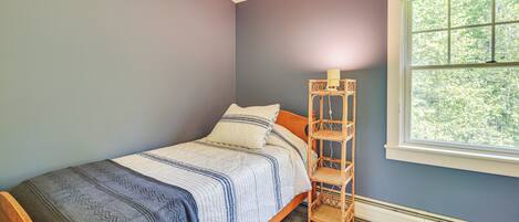 A bedroom with a bed, a nightstand, a window, and a wall-mounted shelf.