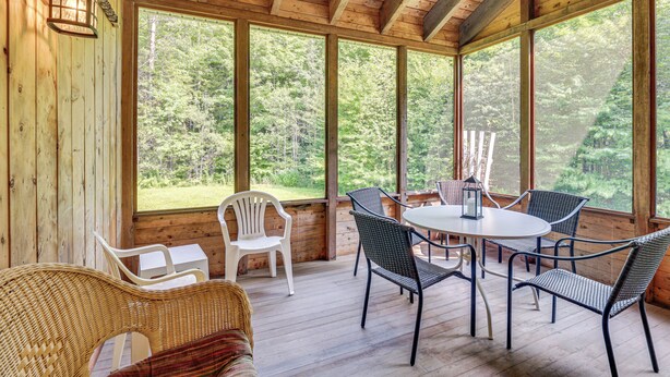A wooden deck with a round table and chairs, large windows, and a wicker chair. - Rural Retreat 3 Mi to Morrisville & Rail Trail! (Hyde Park)