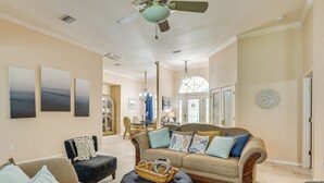 Un salon spacieux avec un grand canapé, un pouf et un ventilateur de plafond.