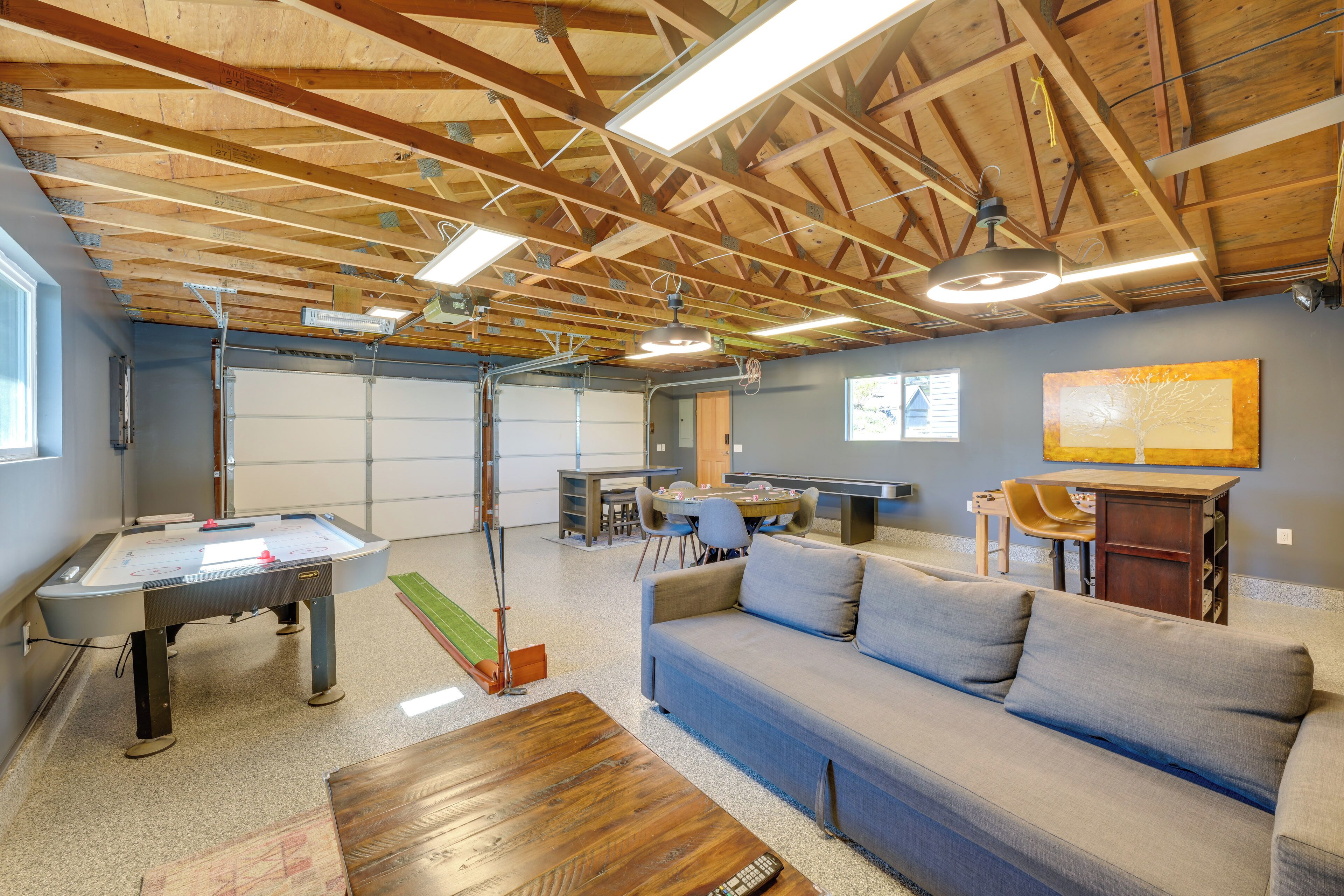 A spacious room with a pool table, a sofa, a dining table with chairs, and a basketball hoop.