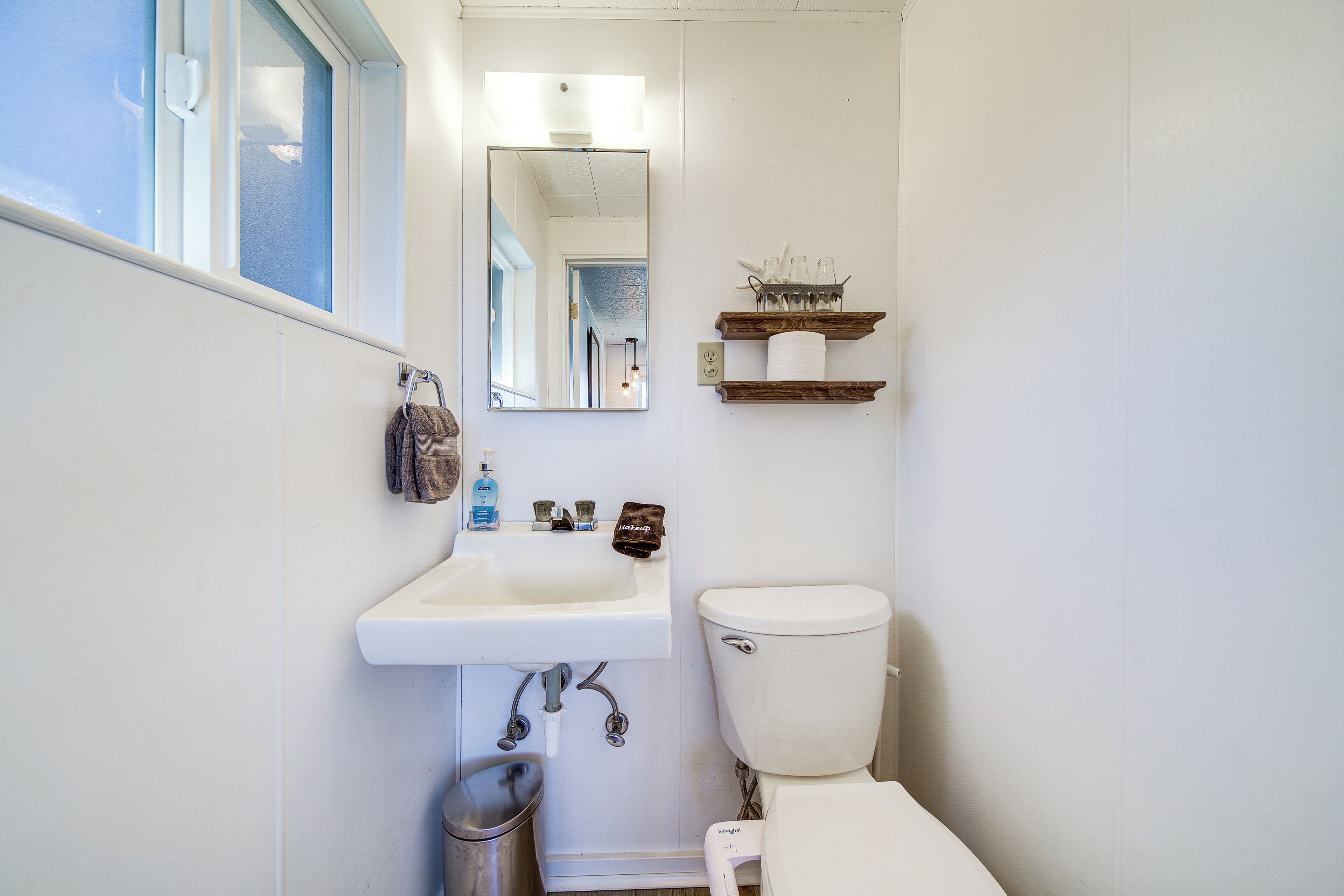 A bathroom with a white sink, a toilet, a mirror, and a shelf with toiletries.