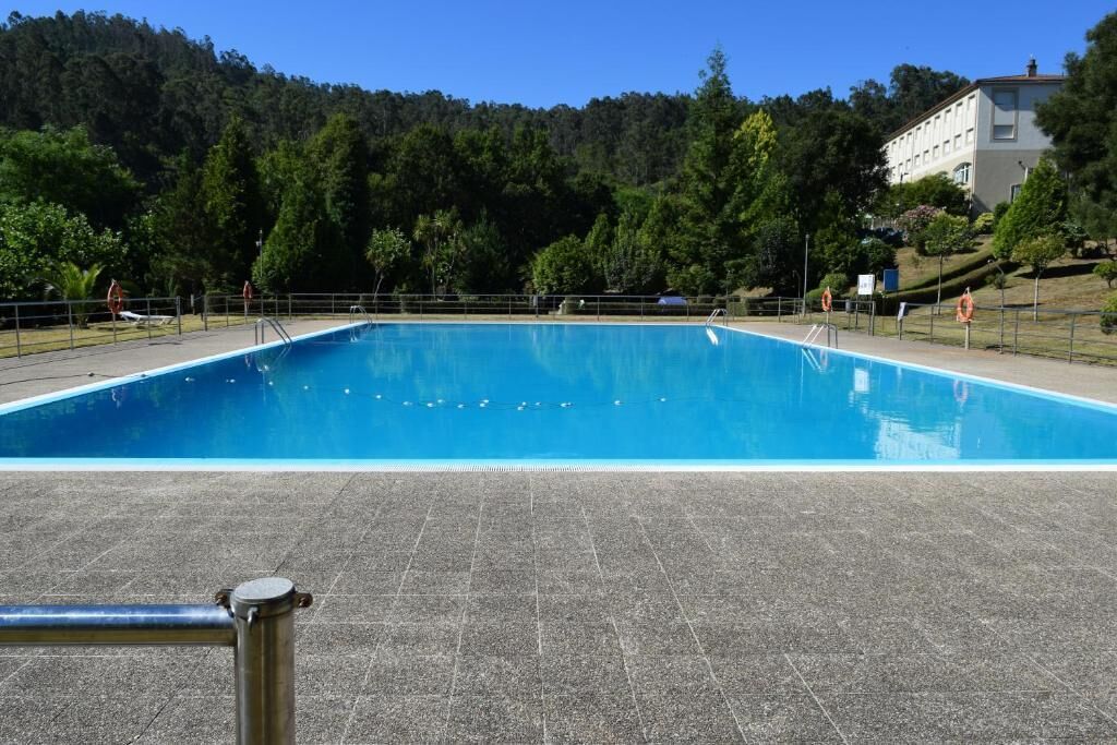 Una piscina rectangular con un patio de baldosas al frente.