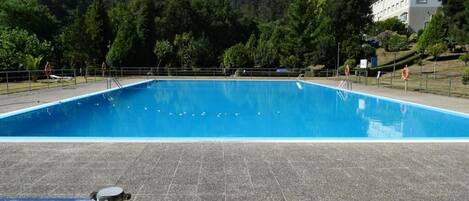 Una piscina rectangular con un patio de baldosas al frente.