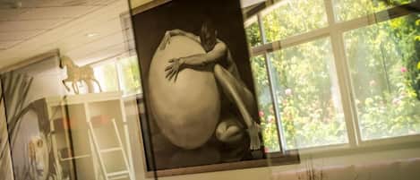 A mural with a human figure embracing a large sphere, a horse sculpture, and a window with a view of greenery.