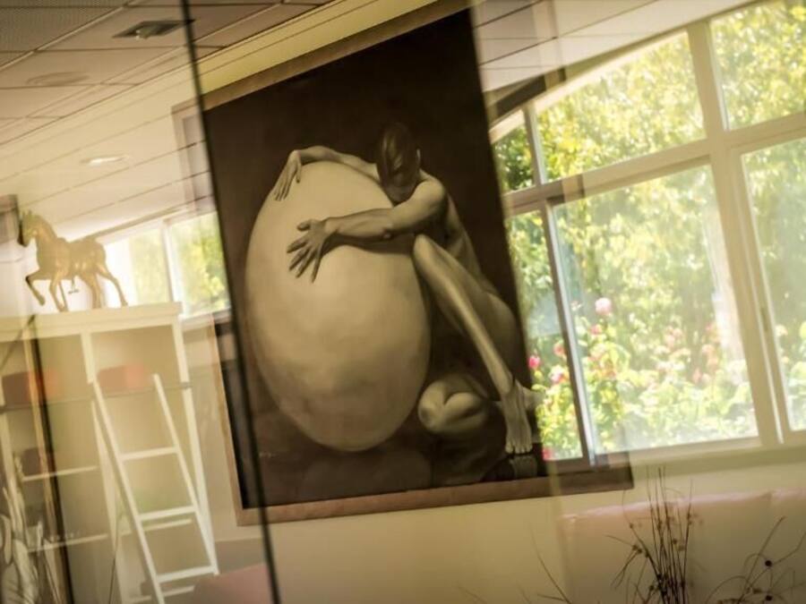 Un mural con la figura de una persona abrazando una esfera grande, una escultura de caballo y una ventana con vistas a zonas verdes.