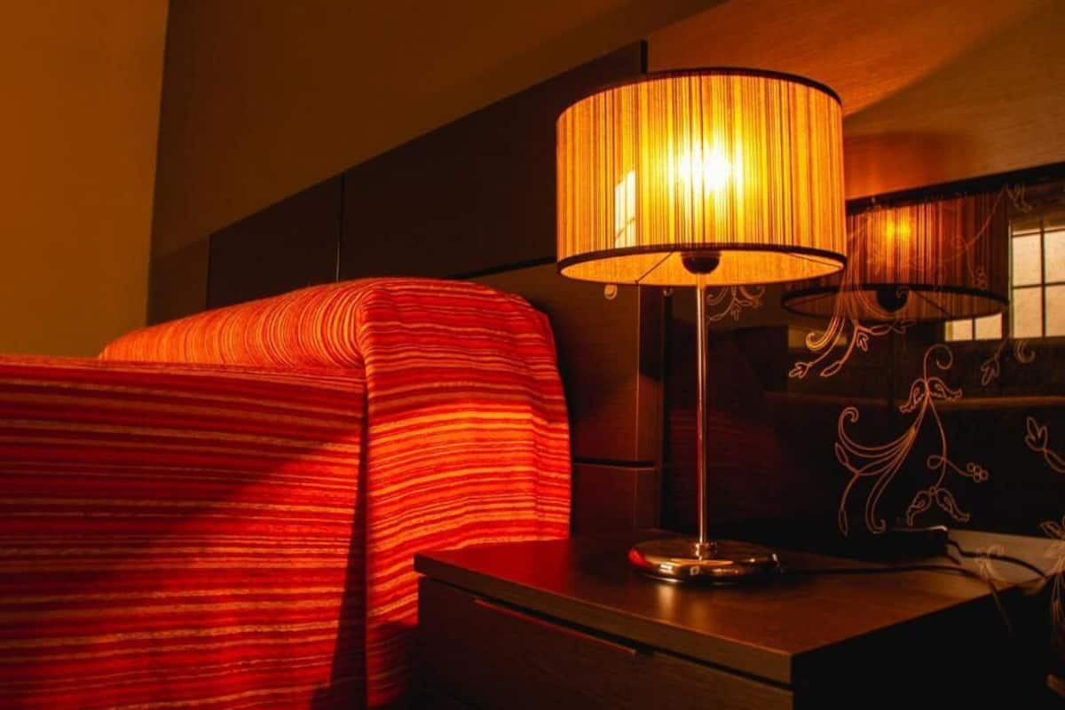 Een hotelkamer met een bed voorzien van een rood gestreepte deken, een nachtkastje met een lamp en een decoratief hoofdbord.