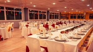 Een balzaal met lange tafels gedekt voor een formeel evenement, met witte tafelkleden en rode accenten.
