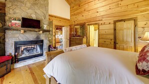 A cozy log cabin bedroom with a stone fireplace, wooden ceiling, and a large bed. - Panoramic Mountain Views & Decks: Franklin Cabin! (Franklin)