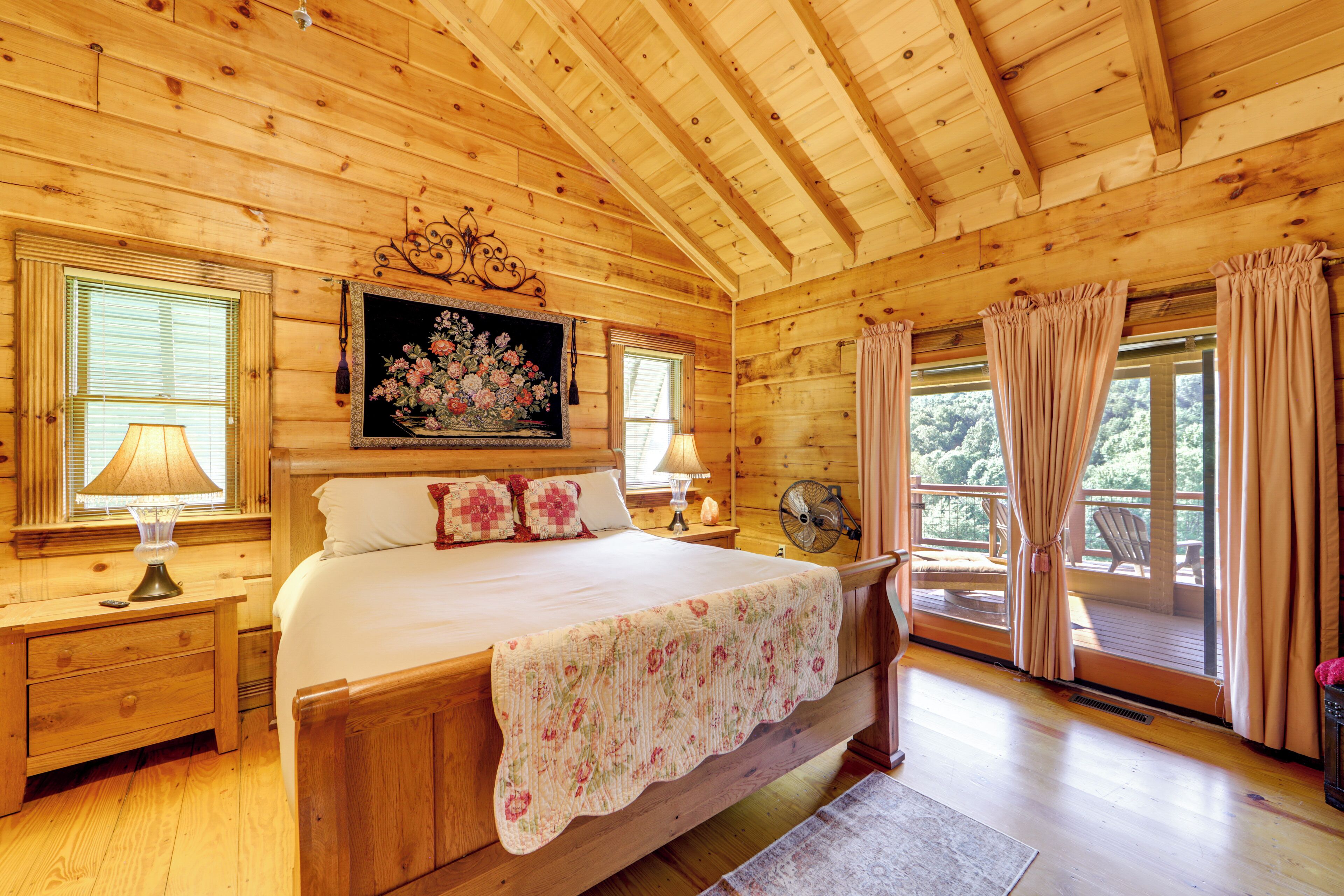 A wooden cabin bedroom with a bed, nightstands, a dresser, a window with curtains, and a balcony.