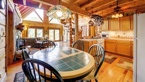 A spacious wooden cabin with a dining area featuring a round table and chairs, a kitchen with wooden cabinets, and a large stained glass window providing natural light. - Panoramic Mountain Views & Decks: Franklin Cabin! (Franklin)