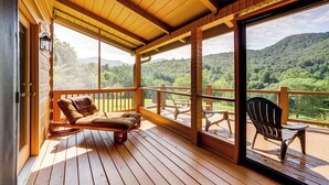 A wooden deck with a cushioned chair and a table, overlooking a forested hillside. - Panoramic Mountain Views & Decks: Franklin Cabin! (Franklin)