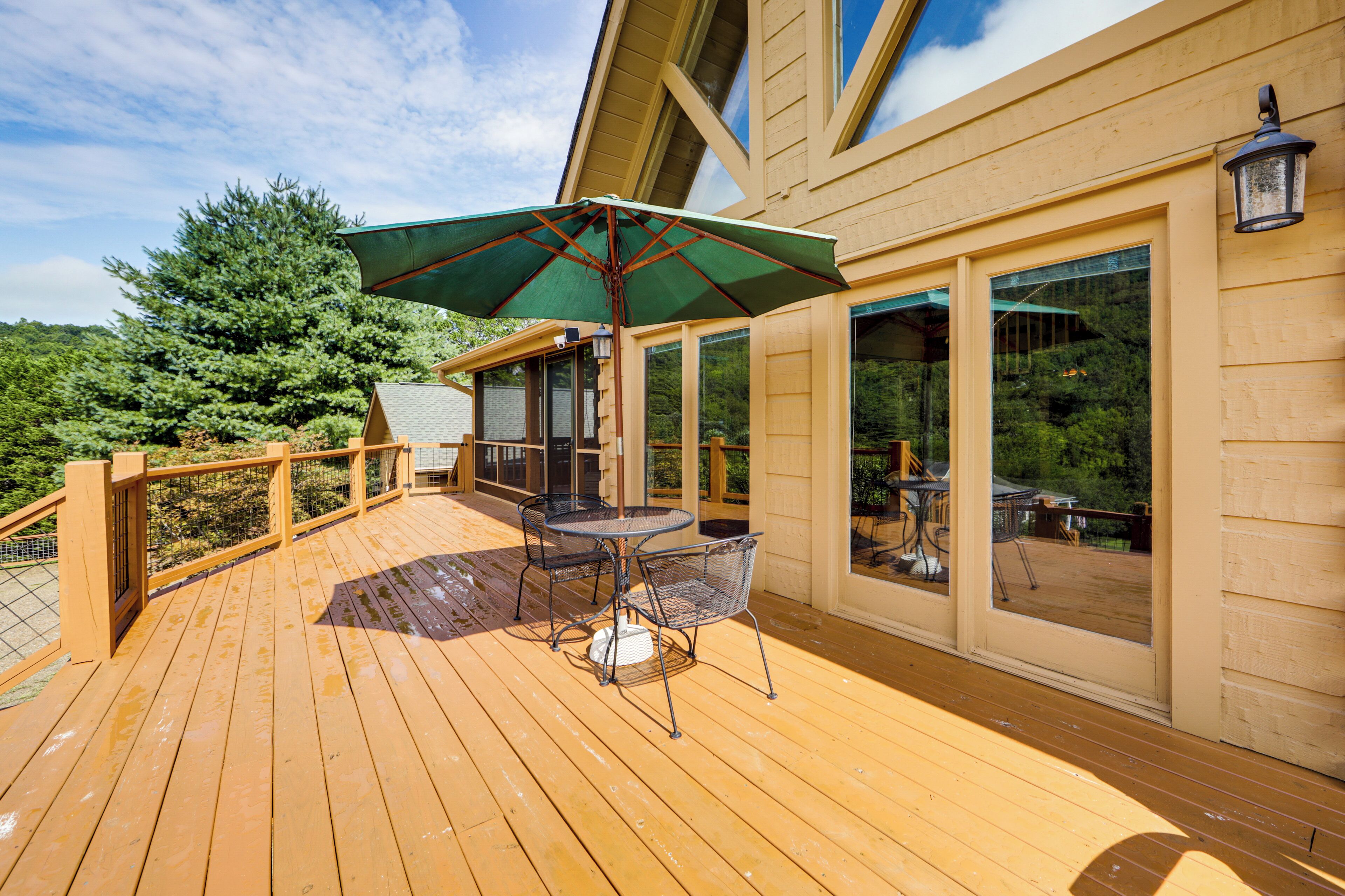 A wooden deck with a table and chairs, a green umbrella, and a view of a forested area.