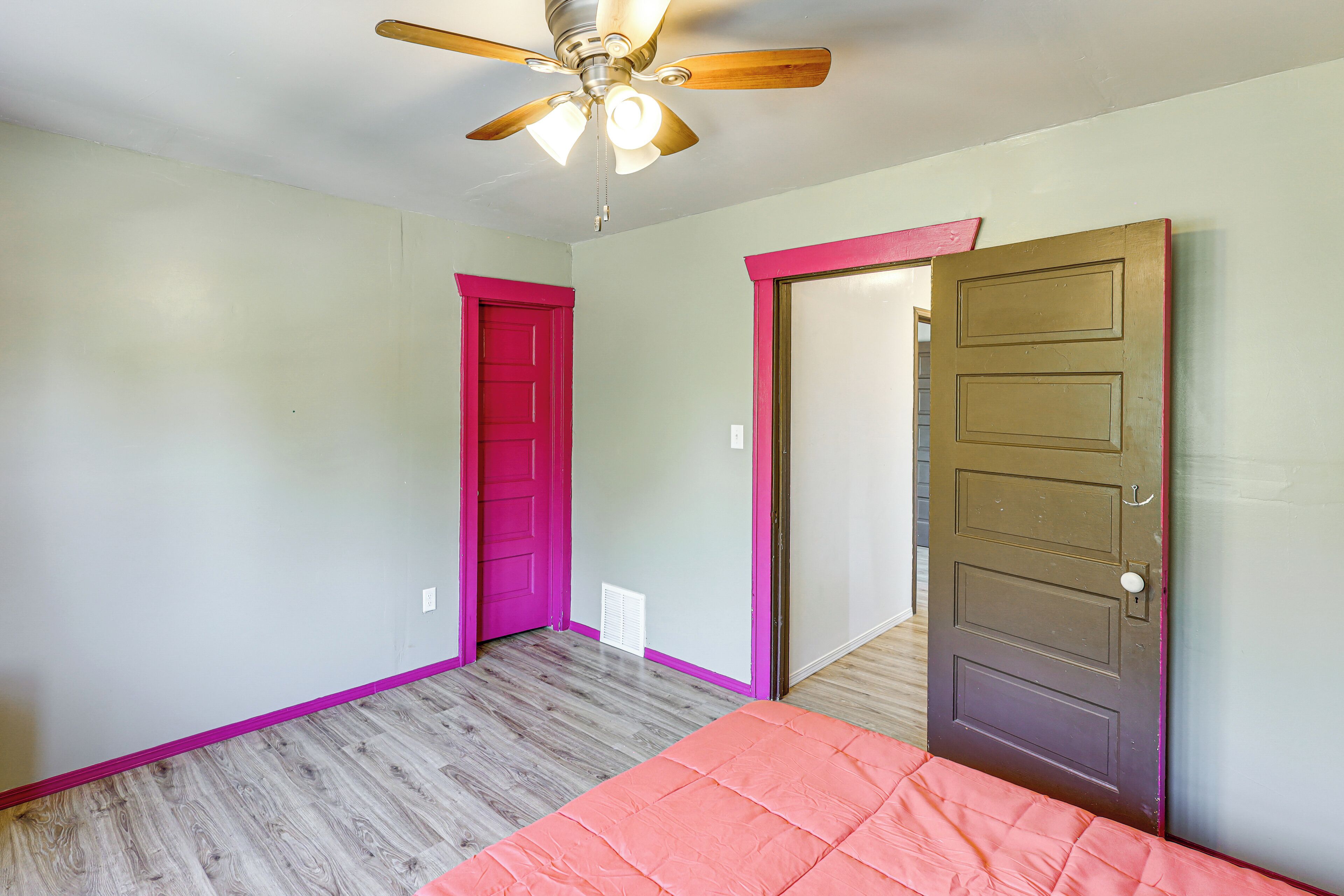 A bedroom with a ceiling fan, two doors, and a bed with a pink bedspread.