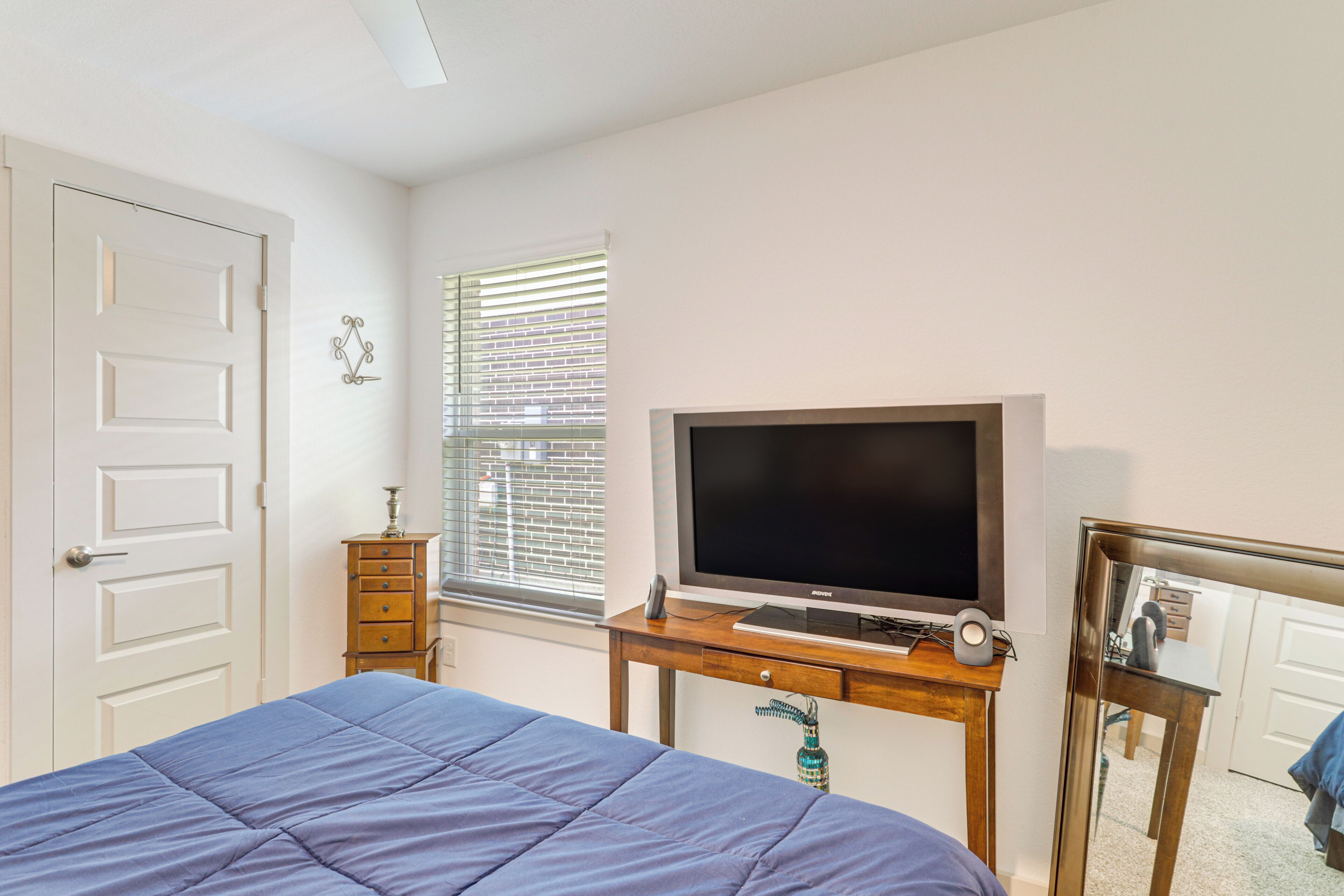 A bedroom with a bed, a TV, a dresser, and a window with blinds.