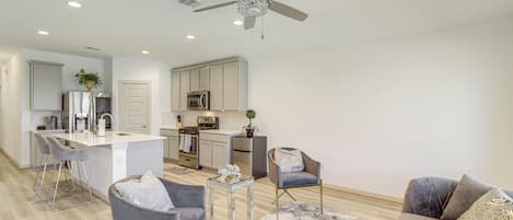 A modern kitchen with a central island, bar stools, and a ceiling fan.
