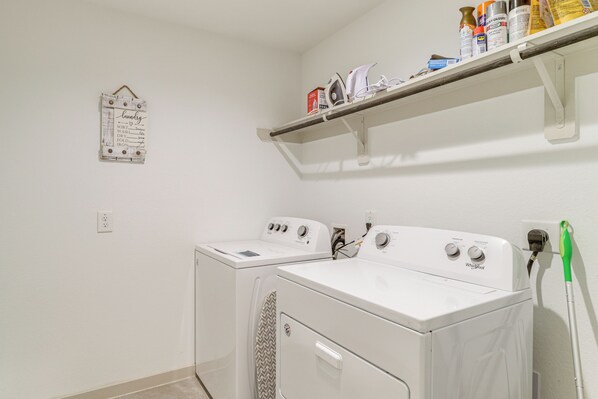 Un espace buanderie comprenant deux machines à laver à chargement frontal, une étagère avec des produits de nettoyage et un panneau affichant les instructions de lavage sur le mur.