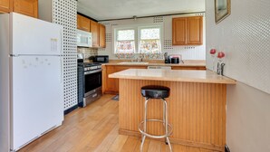 Une cuisine avec des meubles de rangement en bois, un réfrigérateur blanc, un four à micro-ondes, une cuisinière et un tabouret de bar.