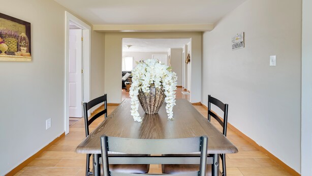 Un coin repas avec une longue table en bois, des chaises noires et un vase rempli de fleurs blanches.