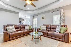 A living room with two brown leather sofas, a glass coffee table, and a ceiling fan.