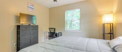 A bedroom with a bed, a dresser, a desk, a chair, a ceiling fan, and a window.