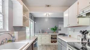 A modern kitchen with white cabinetry, a stainless steel sink, and a glass-top stove. - Game, Swim & Explore: Family Home in Pensacola (Pensacola)