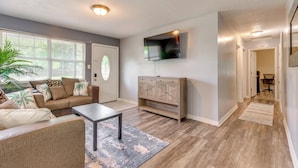 A spacious living room with a sofa, coffee table, and TV mounted on the wall. - Game, Swim & Explore: Family Home in Pensacola (Pensacola)