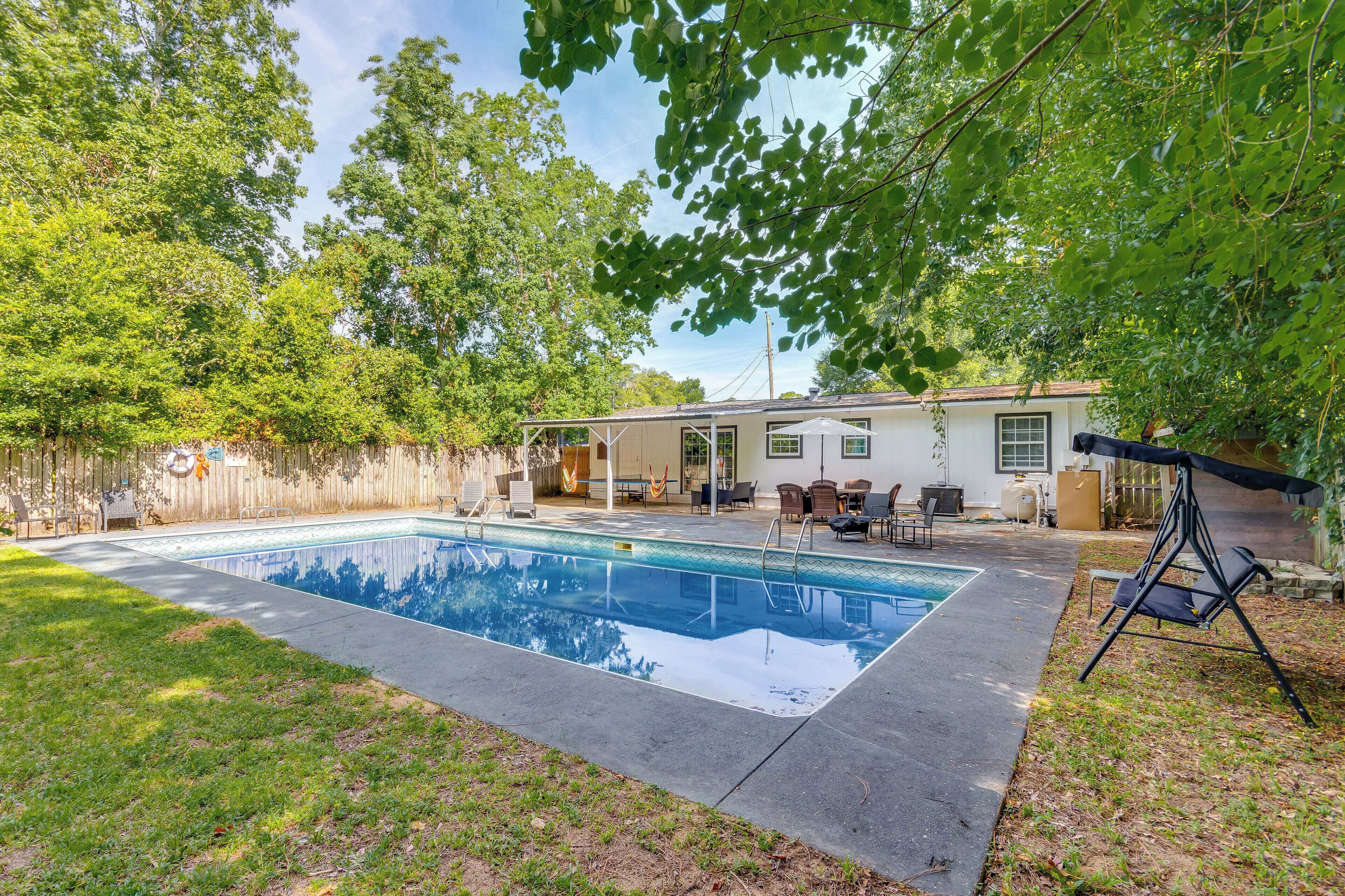 A backyard with a swimming pool, a patio with outdoor furniture, and a house in the background.