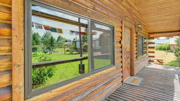 Una cabaña de troncos con ventanas grandes, una terraza de madera y una mesa de picnic.