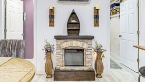A living room with a stone fireplace, a wooden bench, and a round table. - 7 Mi to Kitty Hawk Pier & Beach: Studio w/ Patio! (Harbinger)