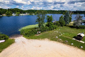 A lakeside property with a sandy beach, a small cabin, and a boat dock. - Waterfront Retreat w/ Dock & Yard in Reed City! (Reed City)