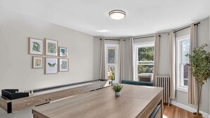 Ein modernes Zimmer mit einem langen Tisch, gerahmten Kunstwerken an der Wand und einem Blumentopf.