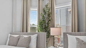 Ein Schlafzimmer mit zwei Betten, einem Nachttisch mit Lampe, einer Topfpflanze und Blick ins Freie.