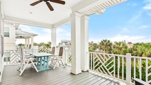 A covered outdoor area with a table and chairs, a ceiling fan, and a view of palm trees and buildings. - Heated Pool Elevator Game Room Ocean Decks (St. Augustine)