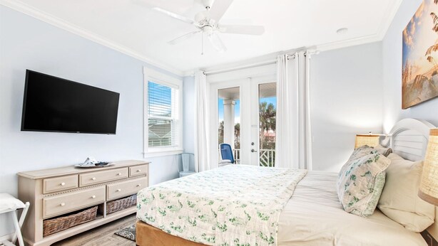 A bedroom with a bed, a TV, a ceiling fan, a window, and a door leading to an outdoor area. - Heated Pool Elevator Game Room Ocean Decks (St. Augustine)