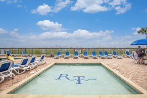 A swimming pool with 'RT' written in the water, surrounded by lounge chairs and a clear sky.