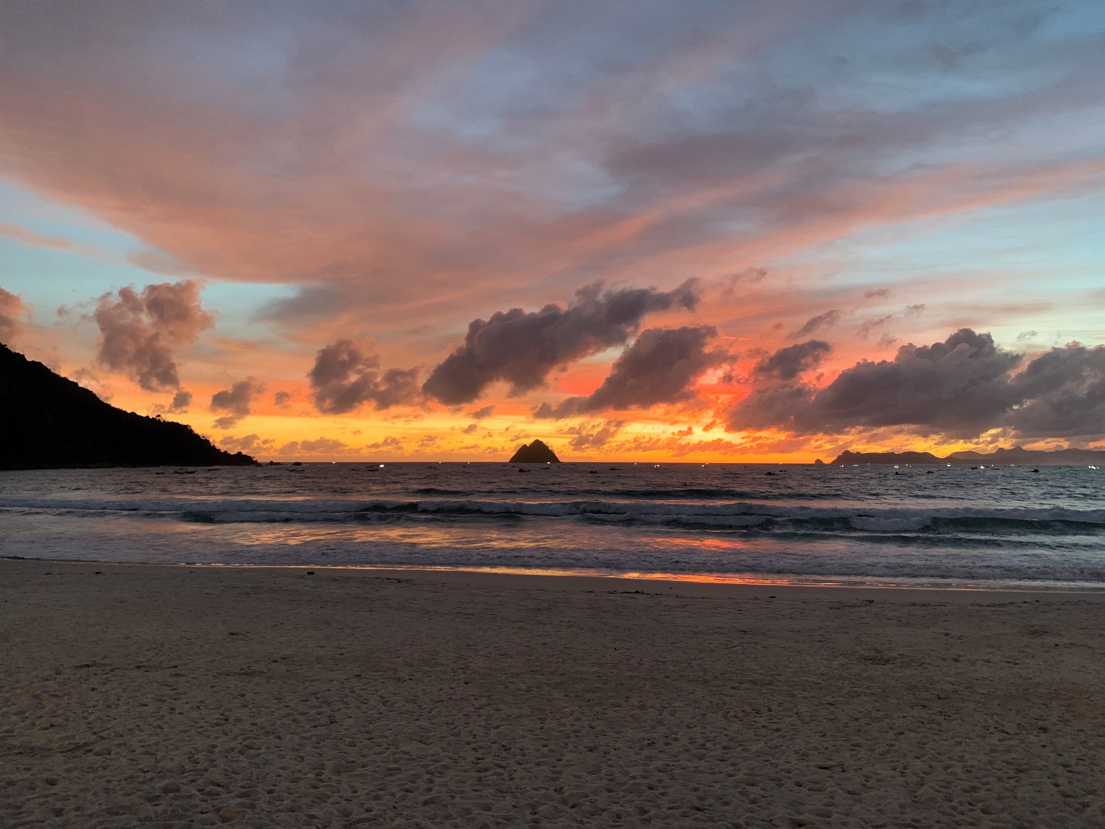 Une plage au coucher du soleil, avec des vagues et une île qui se dessine à l'horizon.