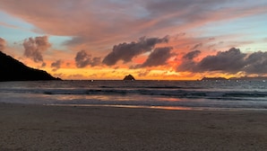 Una playa con un atardecer, olas y una isla distante.