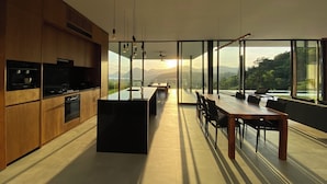 A modern kitchen with a central island, wooden cabinets, and a dining area with a view of mountains. - Villa Monaco • Oceanview Luxury with Private Pool (Selong Belanak)
