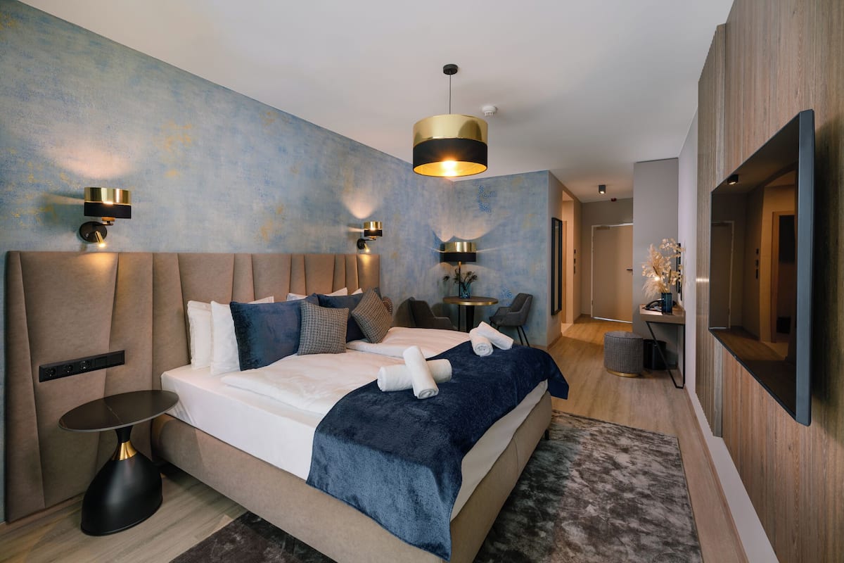 A modern bedroom with a large bed, bedside tables, a TV, and a wall-mounted light fixture.