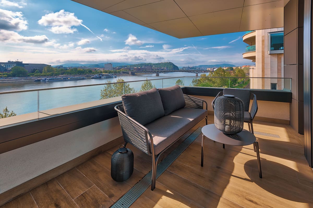 A balcony with a sofa, chair, and a view of a river and cityscape.