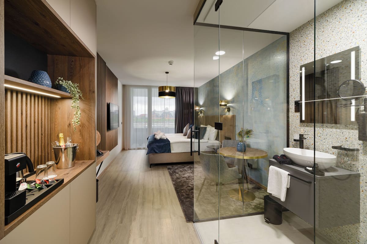 A modern bedroom with a bed, bedside table, and a glass-enclosed bathroom with a sink and mirror.