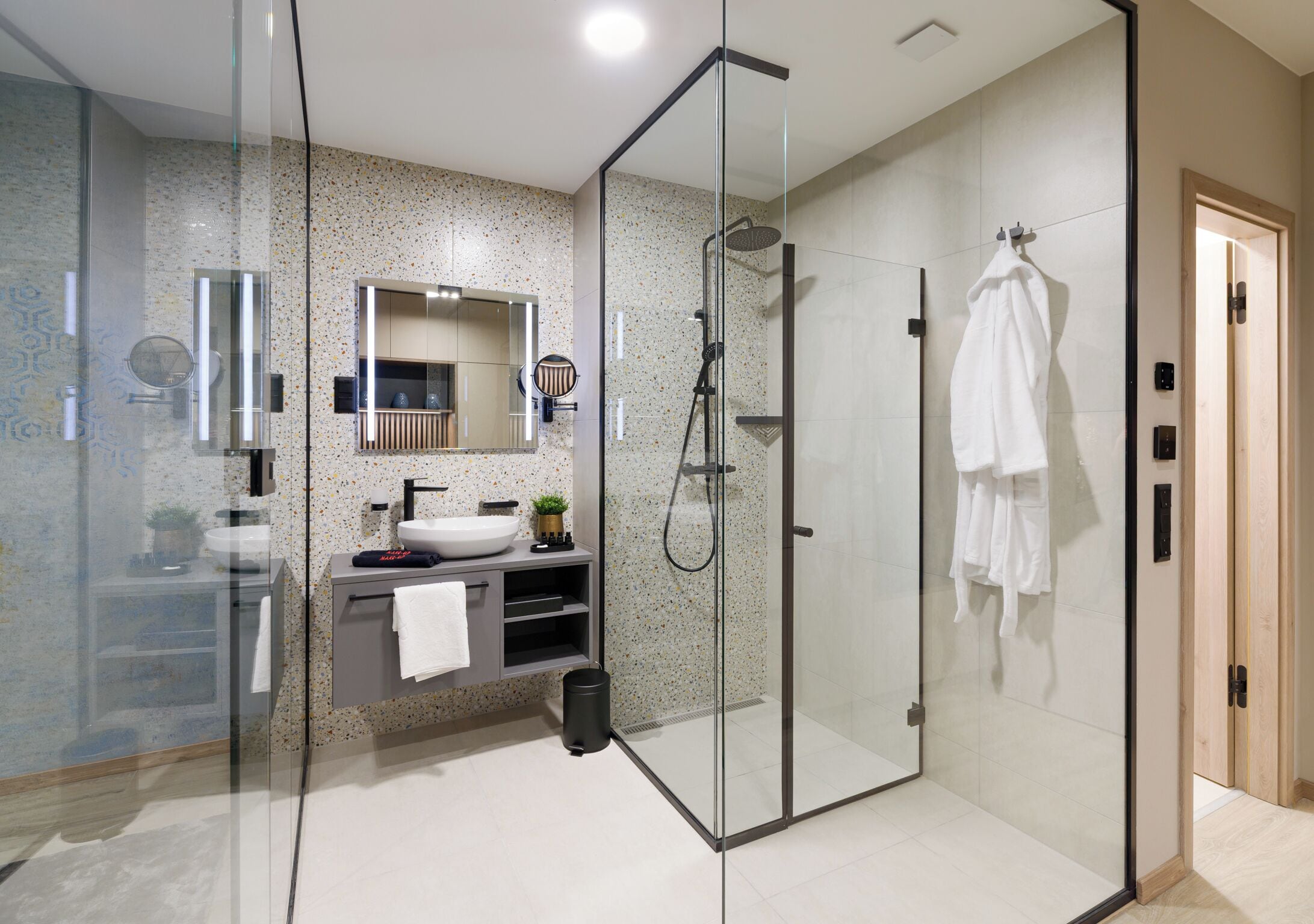 A modern bathroom with a glass-enclosed shower, a sink with a mirror above it, and a towel rack with towels.