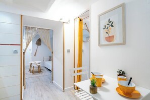 Een kamer met een witte tafel, gele stoelen, een kleine plant en een lijst met een afbeelding aan de muur.