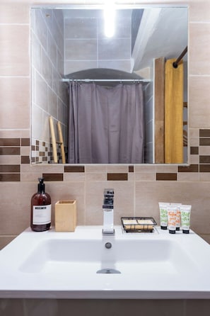 A bathroom with a sink, mirror, shower curtain, and toiletries.