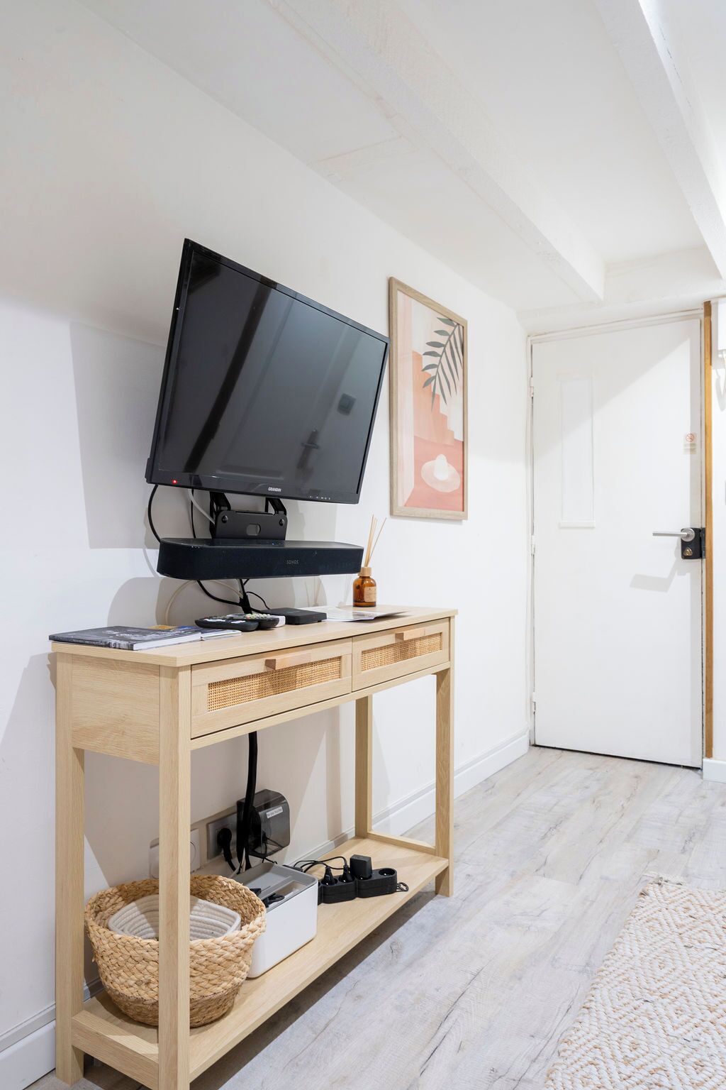 A room with a television on a wooden stand, a door, and a framed picture on the wall.