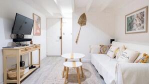 Un salon moderne avec un téléviseur, une console en bois et un canapé blanc agrémenté de coussins à motifs.