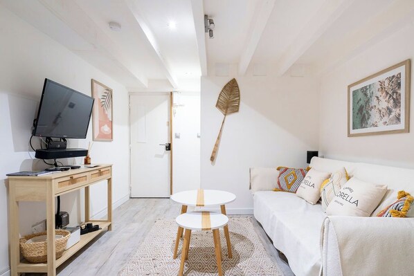 A modern living room with a TV, wooden console, and a white sofa with patterned cushions.