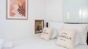 Une chambre d’hôtel avec un lit, des oreillers blancs ornés du mot « Cannes », un tableau encadré et une petite œuvre d’art encadrée.
