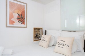 A hotel room with a bed, white pillows with 'Cannes' text, a framed picture, and a small framed artwork. - Le Mimosa mignon en plein centre-ville (Cannes)